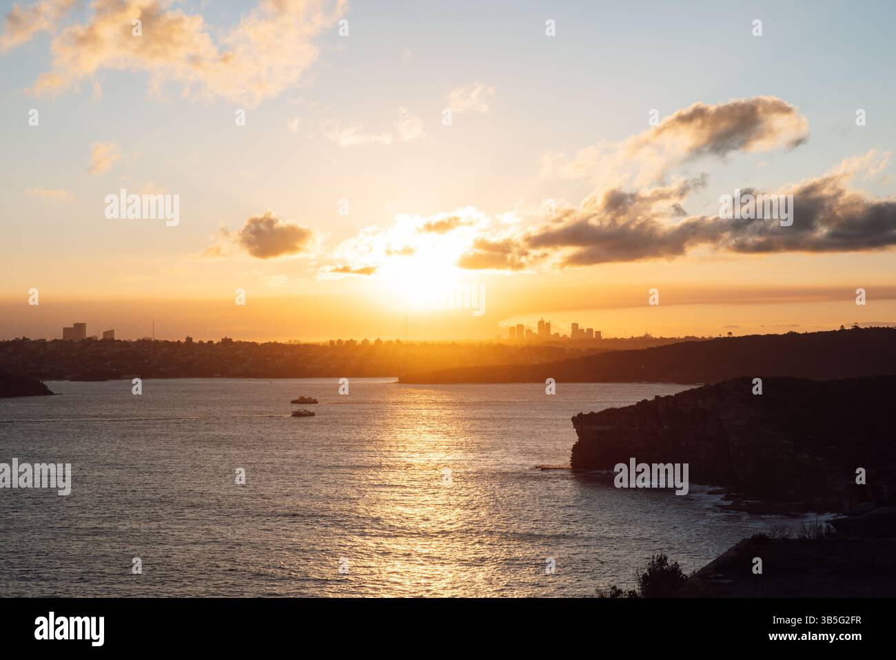 Vista del tramonto sulle scogliere oceaniche e sullo skyline di North Sydney in lontananza Foto Stock