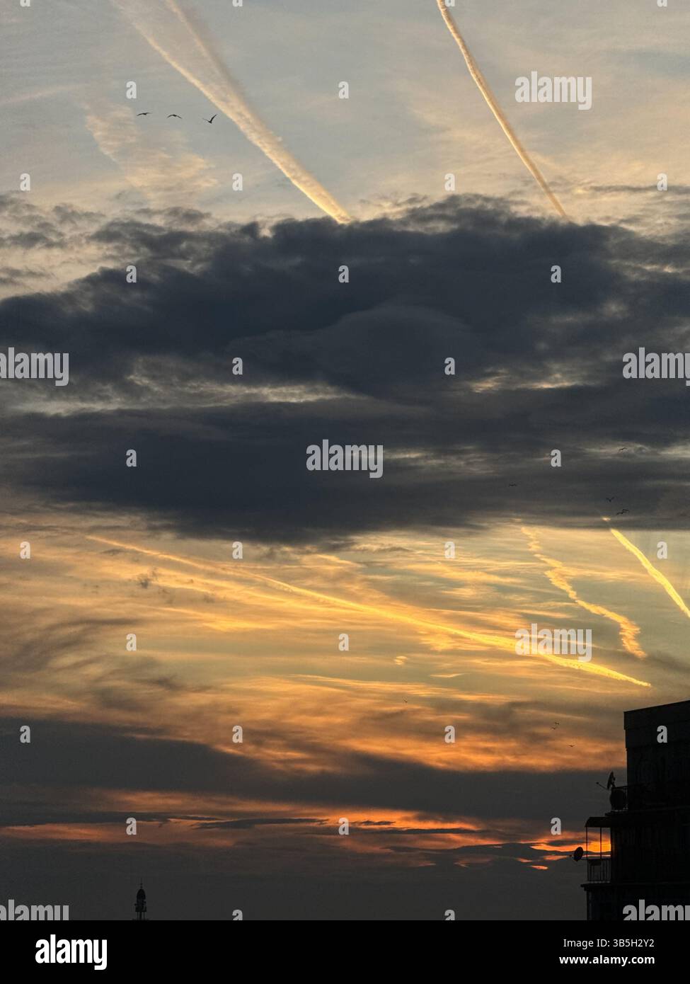 Questa foto mostra un cielo serale con un mix di nuvole scure e chiare, diversi contrafforti di aerei visibili e il caldo gradiente di un tramonto. Qualche uccello Foto Stock