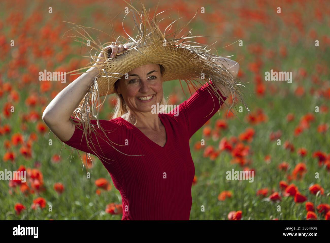 Una donna sorridente con un grande cappello di paglia si trova in un prato papavero, Unterallgaeu, Baviera, Germania, Europa Foto Stock