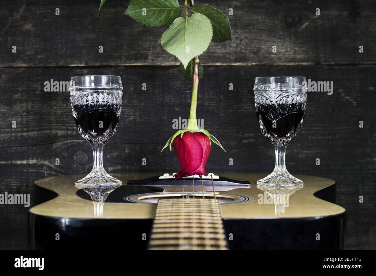 Red Rose e bicchieri di vino in appoggio su una chitarra acustica con sfondo di legno Foto Stock