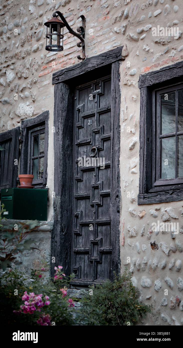 Affascinante porta in legno antica con una struttura in legno, adagiata in uno storico edificio in pietra. Scalini in pietra conducono all'ingresso, adornati da fiori vivaci. Foto Stock