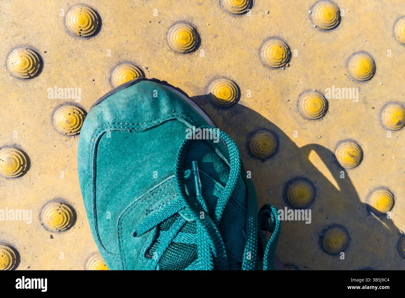 Scarpe verdi su pavimentazione tattile per la sicurezza dei pedoni Foto Stock
