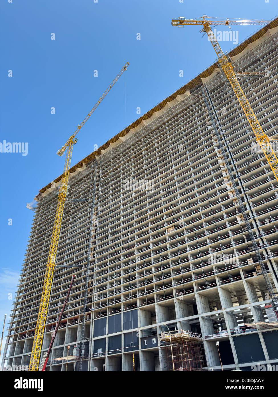 Vista verticale dell'alto edificio in costruzione con struttura in cemento e gru a torre contro il cielo limpido. Sviluppo urbano, nessuna gente. - Immagine stock catturata con smartphone