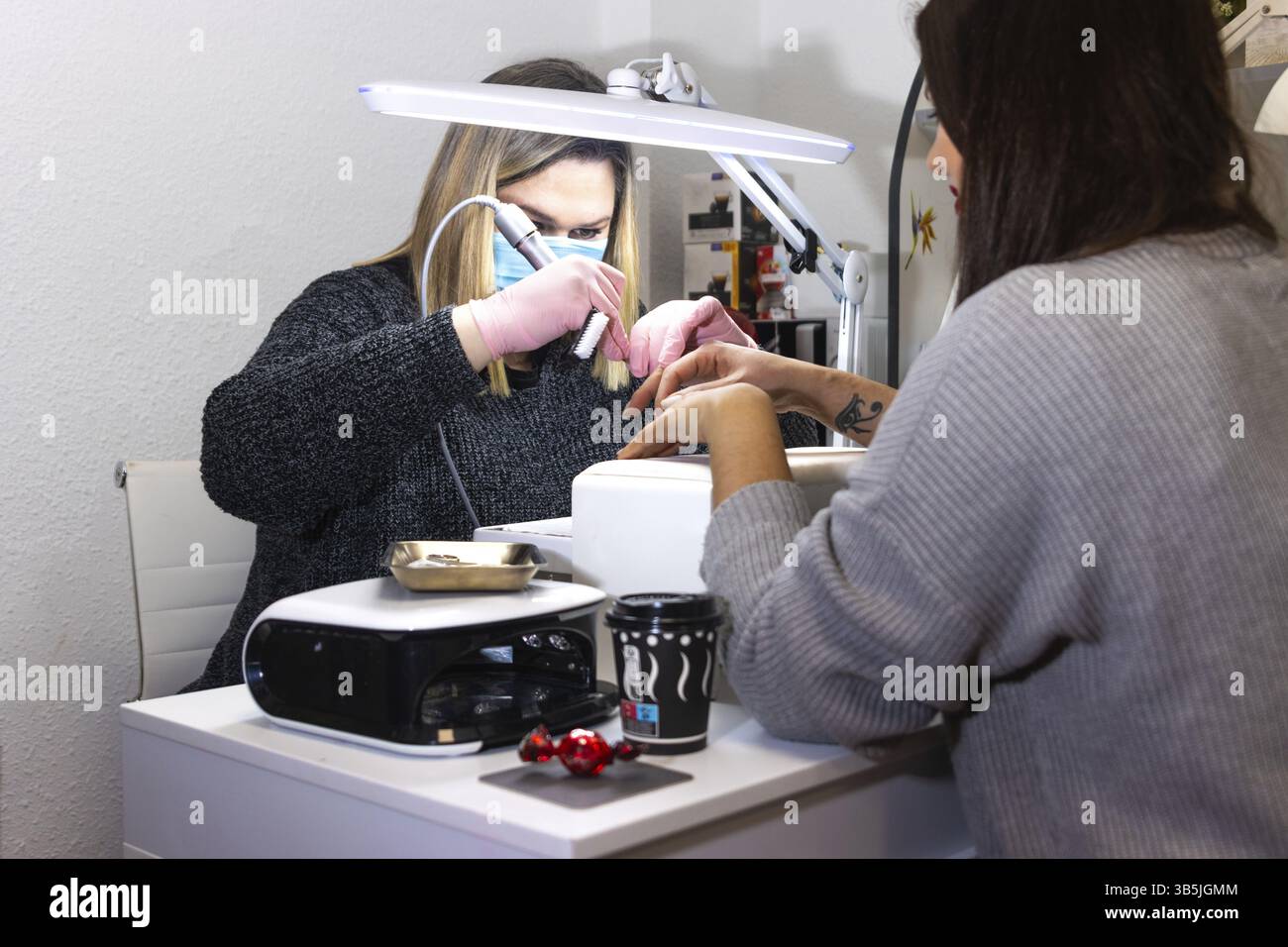 Un chiodo tecnico che indossa una maschera lavora sulle unghie del cliente utilizzando strumenti professionali da salone Foto Stock