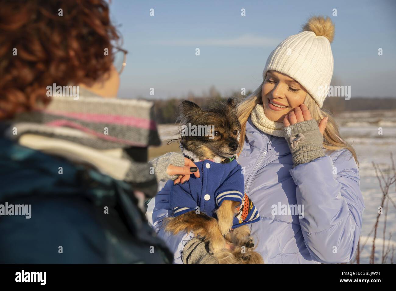 Una figura sfocata di una donna che punta la mano a un cane e la accarezza. L'altra donna, nel frattempo, sta tenendo il cane tra le braccia, il cane è indossato Foto Stock