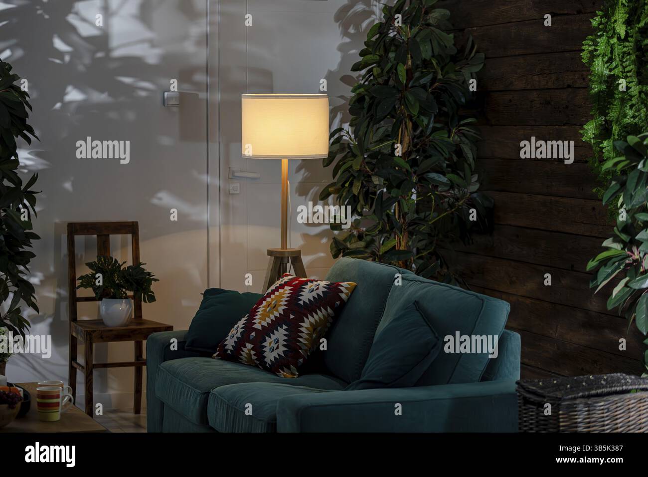 L'elegante e moderno soggiorno è dotato di un comodo divano, immerso tra piante vivaci, impreziosito da un'illuminazione calda e invitante Foto Stock