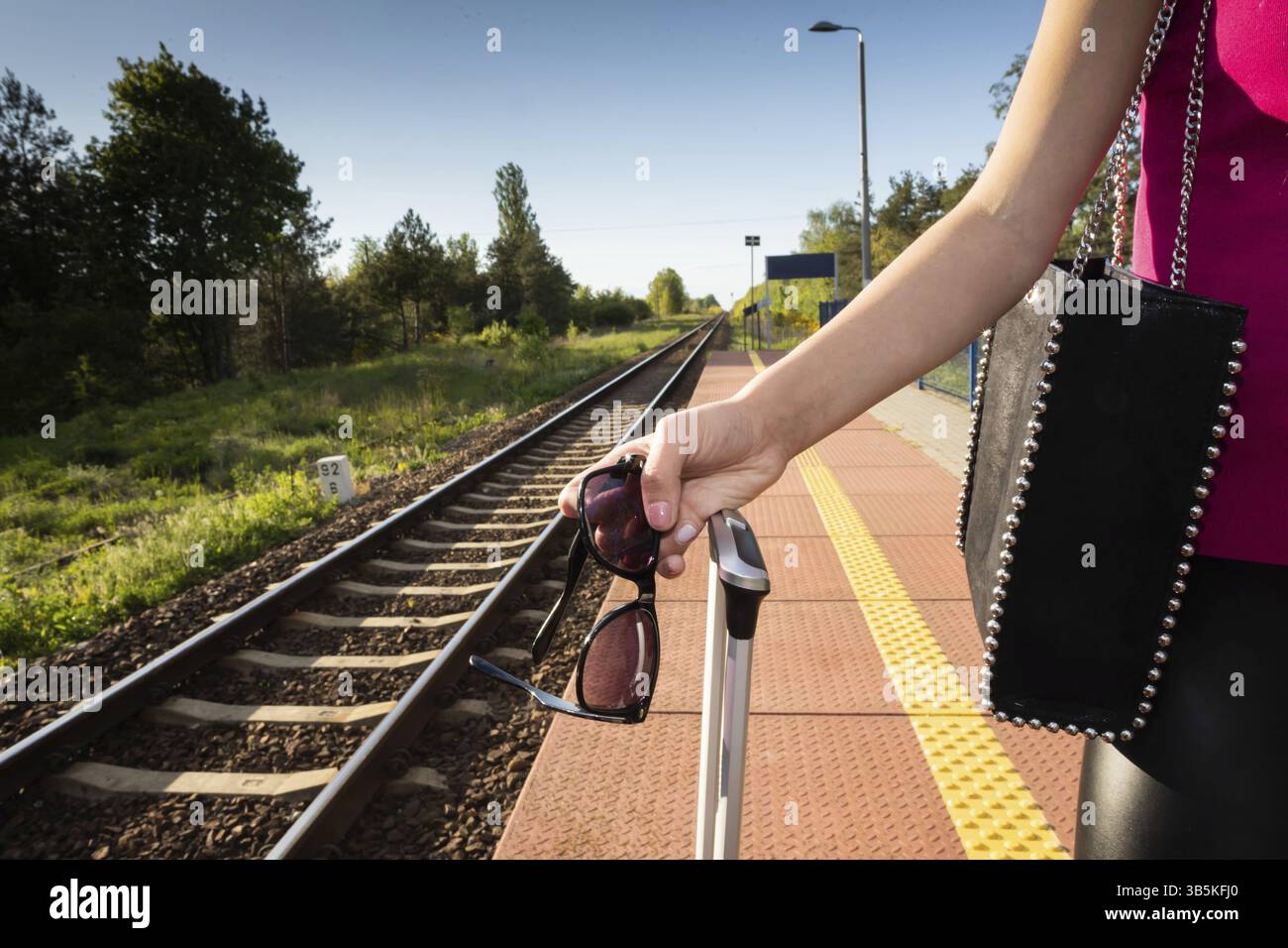 Viaggio in treno estivo. Una donna è in piedi sulla piattaforma ferroviaria e ha in mano gli occhiali da sole Foto Stock