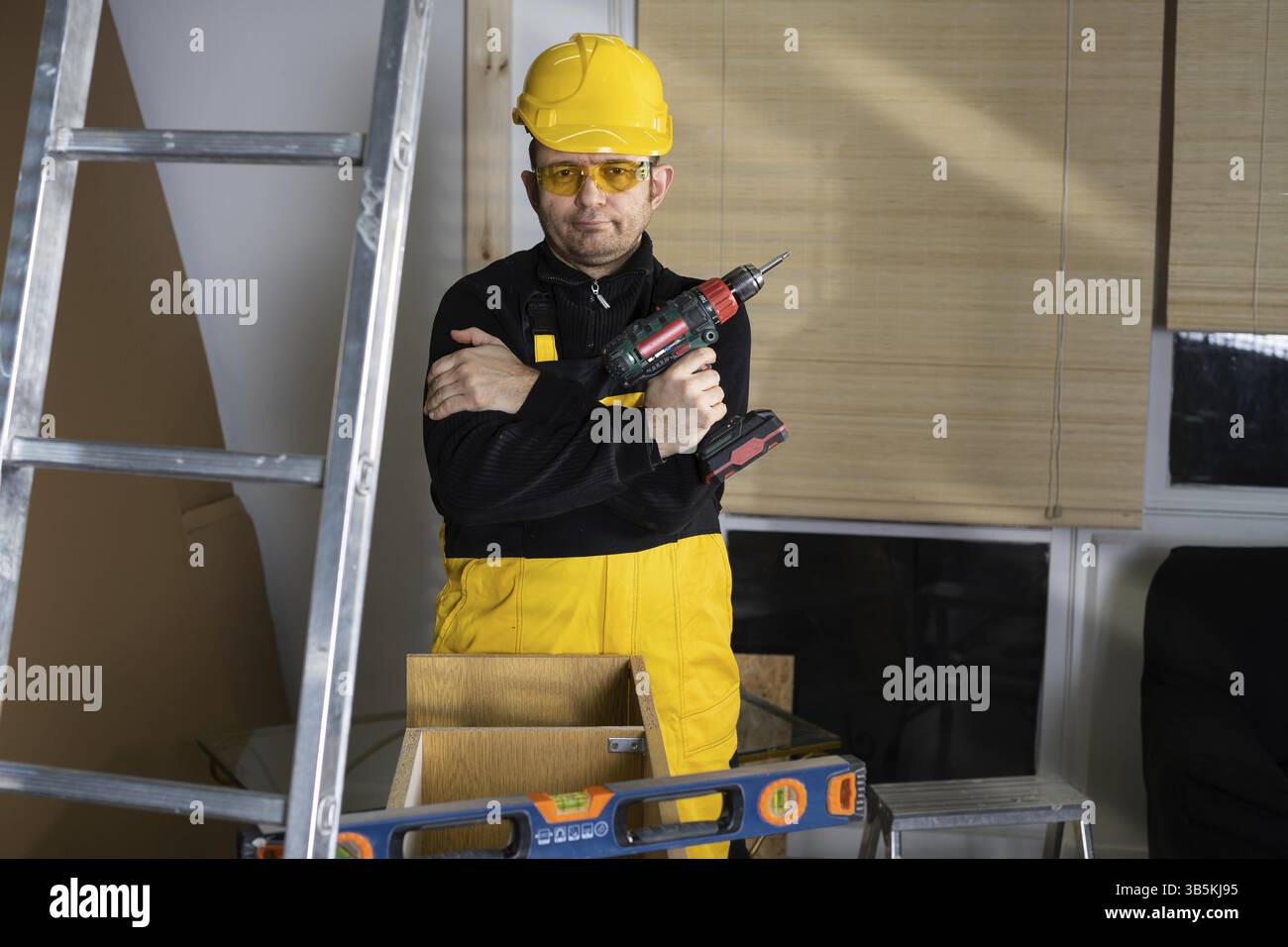 L'operaio edile è in attesa dell'inizio del turno successivo e tiene in mano un cacciavite a batteria. Sorride dolcemente. Un dipendente, il dottor Foto Stock