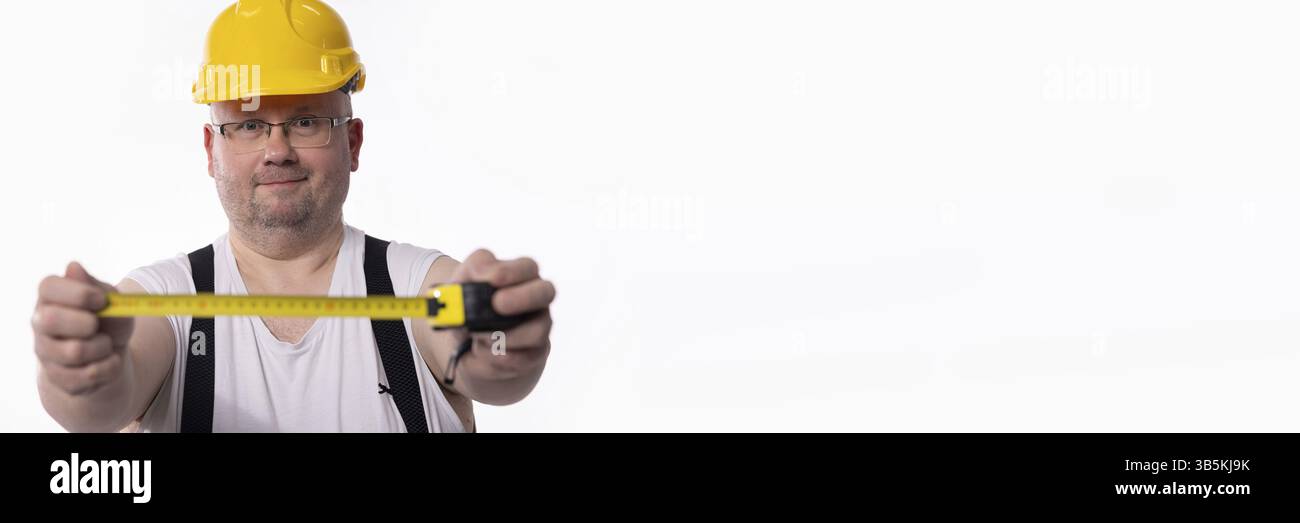 Un operaio edile con un elmetto misura abilmente con un nastro, mostrando la sua esperienza Foto Stock