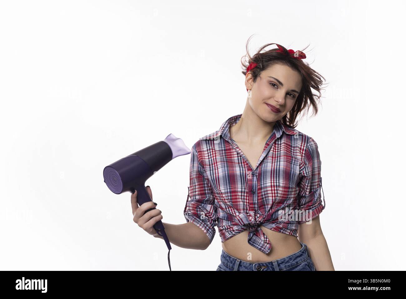 Una donna sicura di sé ed elegante posa giocosa con un asciugacapelli, mostrando le ultime tendenze di moda e bellezza moderne Foto Stock