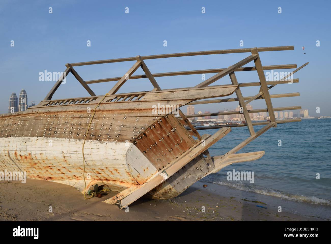 Una barca in sambuco con il tempo si trova abbandonata sulla costa, con costole e scafo in legno che rivelano la tradizionale maestria artigianale del mare arabo Foto Stock