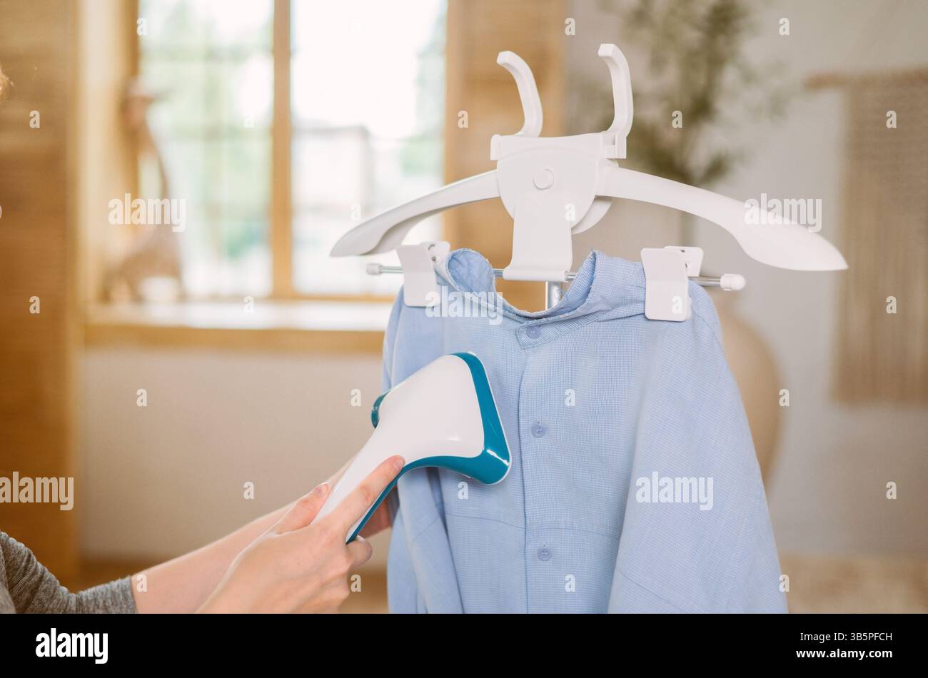 Utilizzo del ferro da stiro a vapore per stirare la camicia in casa. Stirare al vapore per stirare i vestiti a portata di mano Foto Stock