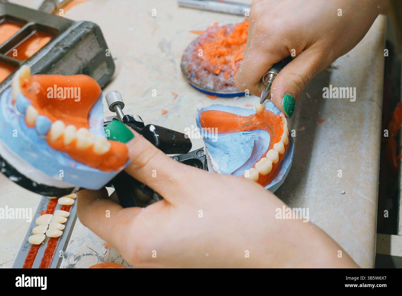 Un odontotecnico esperto smeriglia e forma meticolosamente le protesi utilizzando strumenti specializzati. I colori brillanti dei materiali evidenziano l'intricato de Foto Stock