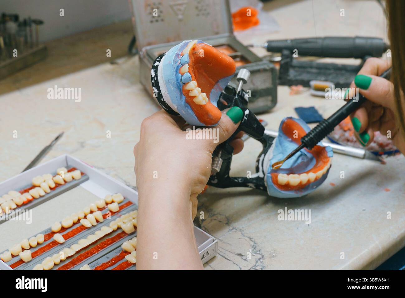 In un laboratorio dentale affollato, un tecnico fora e modella accuratamente le protesi utilizzando cera e utensili specializzati. L'intricato processo mostra la maestria artigianale Foto Stock