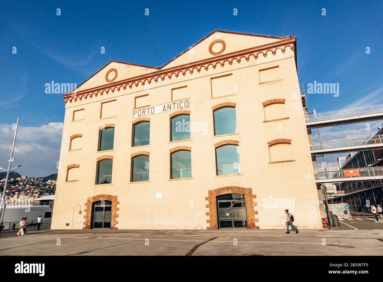 Genova, Italia - 22 settembre 2024: Lungomare di Porto Antico con barche, attrazioni moderne ed edifici storici sotto un cielo limpido. Foto Stock