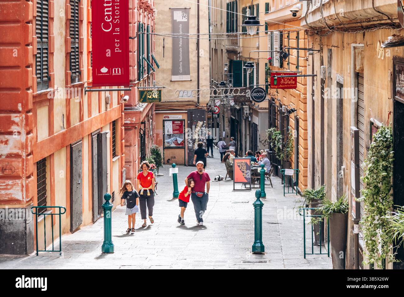 Genova, Italia - 22 settembre 2024: Vivace vicolo medievale con facciate colorate, negozi e caffetterie all'aperto nel centro storico, persone che passeggiano e.. Foto Stock