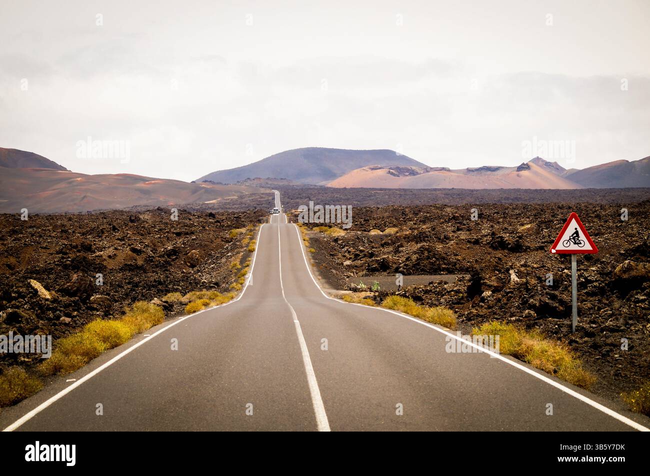 Fotografia paesaggistica di un ambiente vulcanico che mostra il suo suolo roccioso e i colori marrone e ocra e nel mezzo di una strada infinita Foto Stock