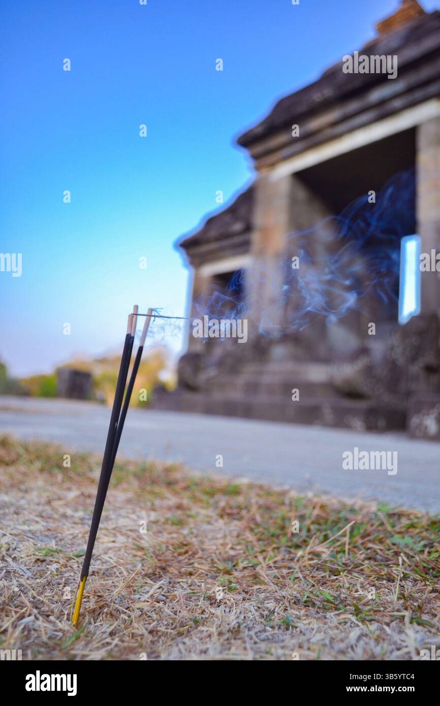 I bastoncini d'incenso si stagliano come sentinelle silenziose nel cortile reale di Ratu Boko, il loro fumo profumato che si snoda tra le antiche rovine del palazzo al crepuscolo. Foto Stock