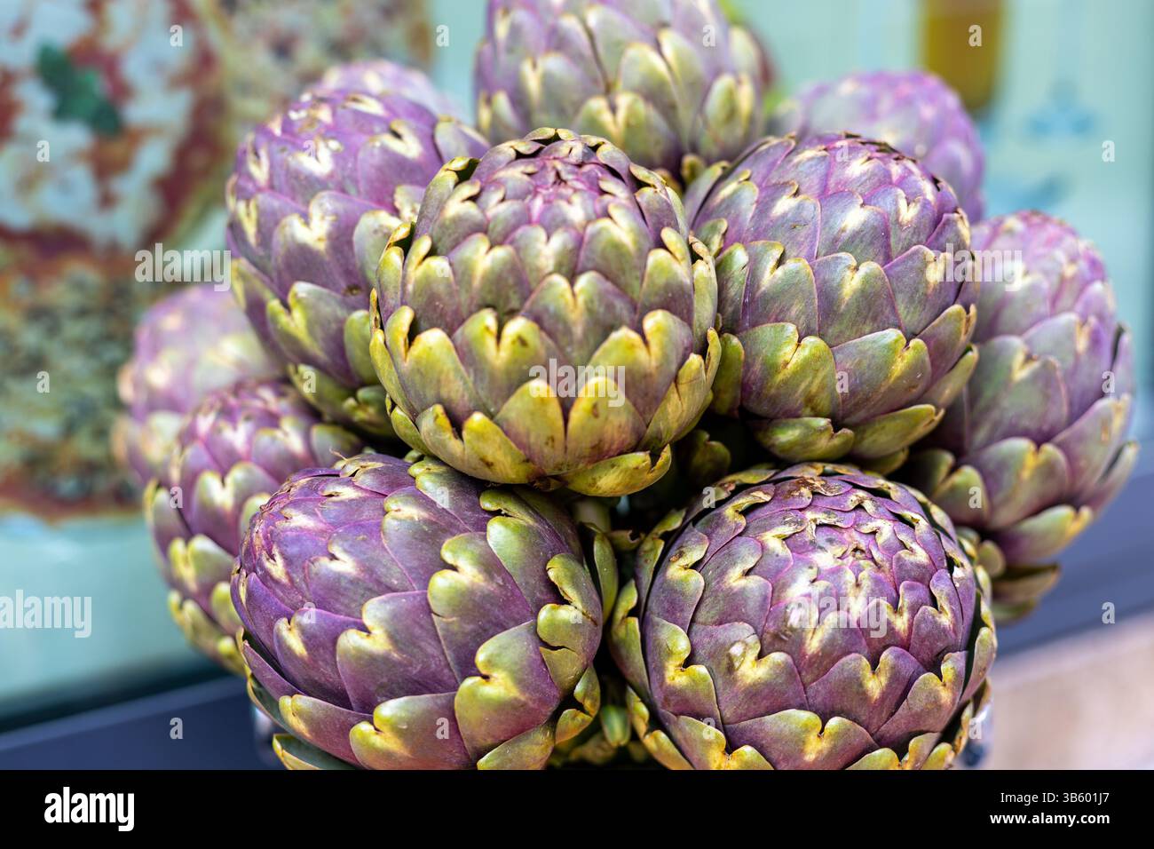 Una vivace mostra di carciofi viola freschi è organizzata in un cestino in un vivace mercato locale. I carciofi sono impilati con cura, evidenziando l Foto Stock