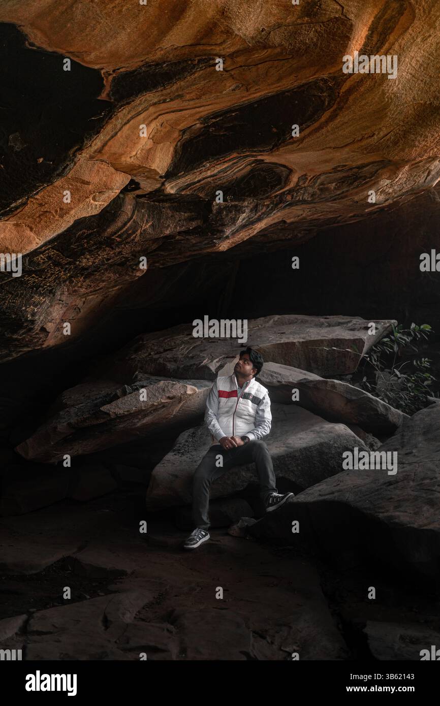 Uomo seduto all'interno della grotta con formazioni rocciose che indossano la giacca bianca avventura viaggi fotografici nella natura. Uomo seduto sotto le formazioni rocciose. Foto Stock