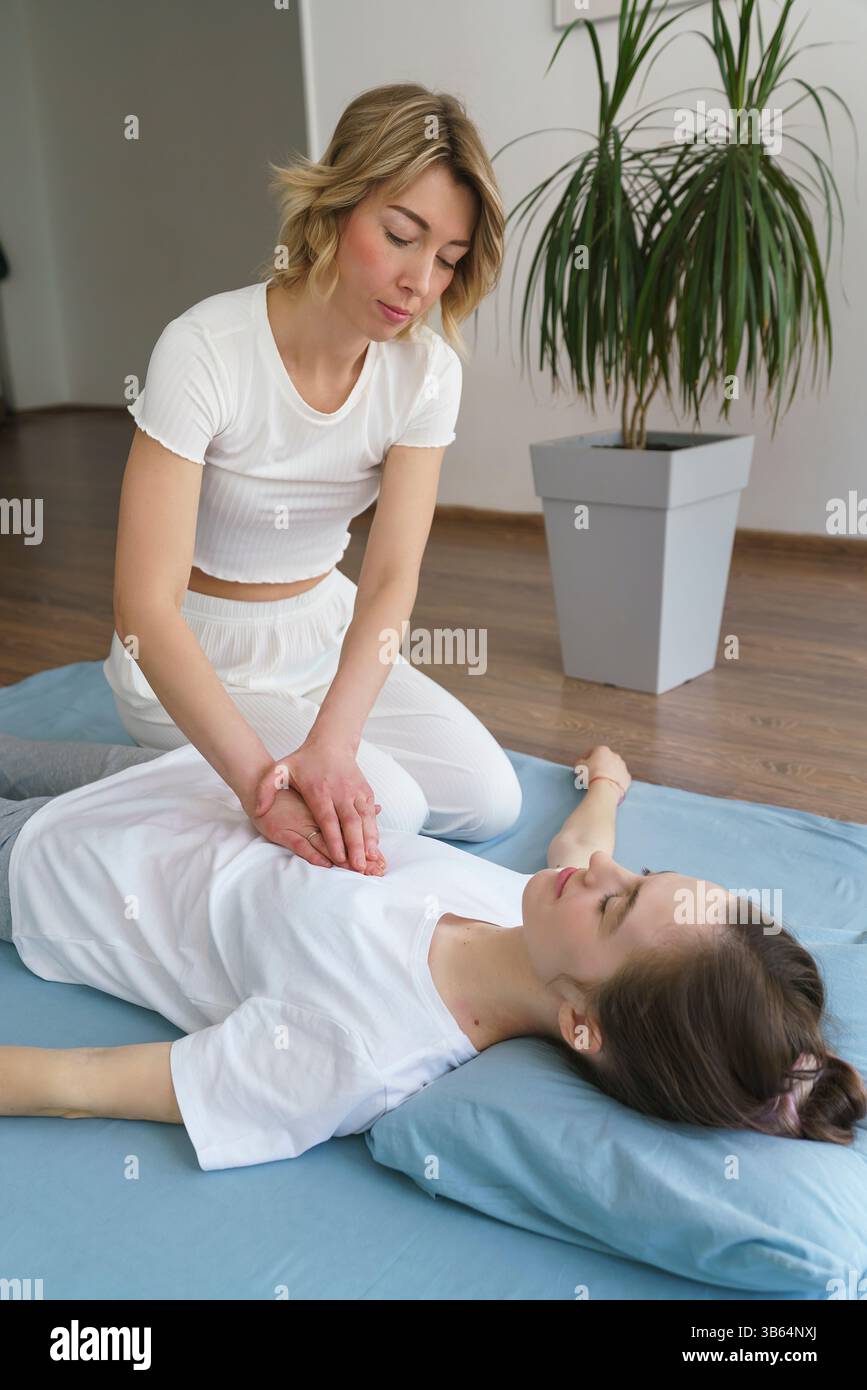 Una giovane massaggiatrice fa un massaggio thailandese sul pavimento massaggiando le articolazioni dell'anca e della pelvi Foto Stock