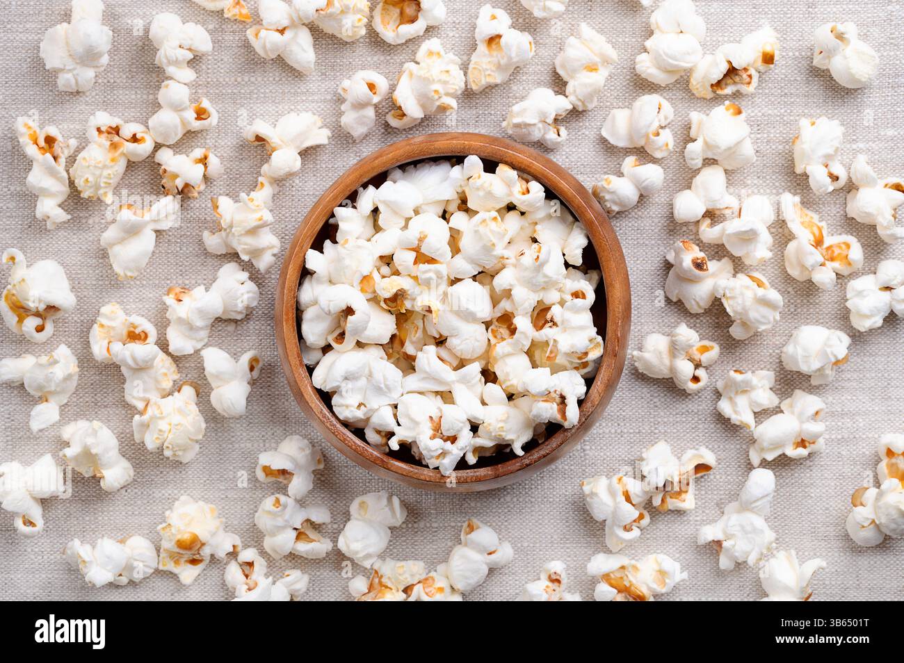 Popcorn fresco, mais in una ciotola di legno e tutto intorno, su tessuto di lino. Semi della varietà Zea mays everta, espansi e gonfiati. Foto Stock