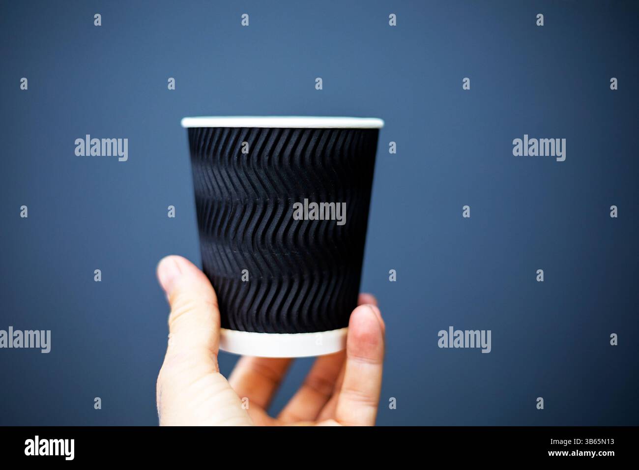 tenendo una tazza monouso nera su sfondo grigio. Mockup per design, loghi, illustrazioni Foto Stock