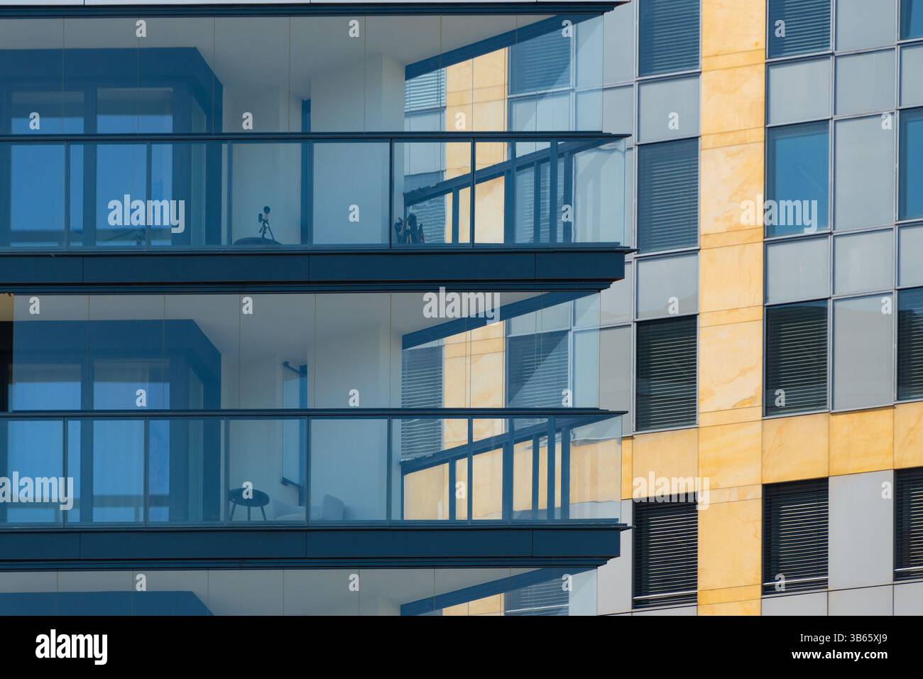 I moderni balconi in vetro rivelano linee architettoniche pulite, in contrasto con la facciata strutturata e colorata dell'edificio adiacente. una città a strati Foto Stock