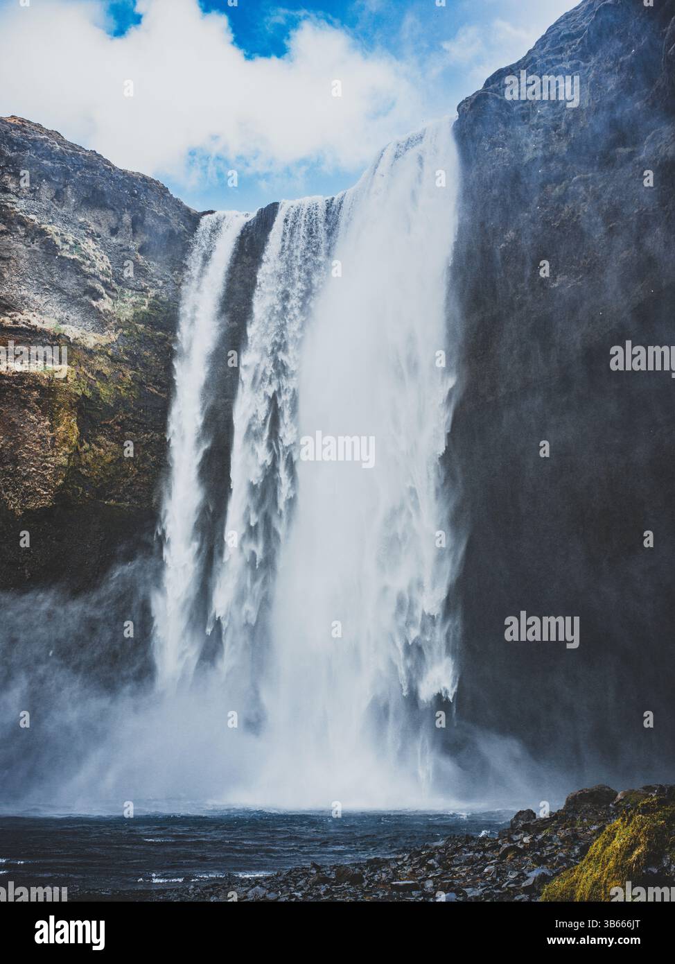 Cascata di Skógafoss che si schianta lungo un'alta scogliera sotto un cielo luminoso, nel sud dell'Islanda Foto Stock
