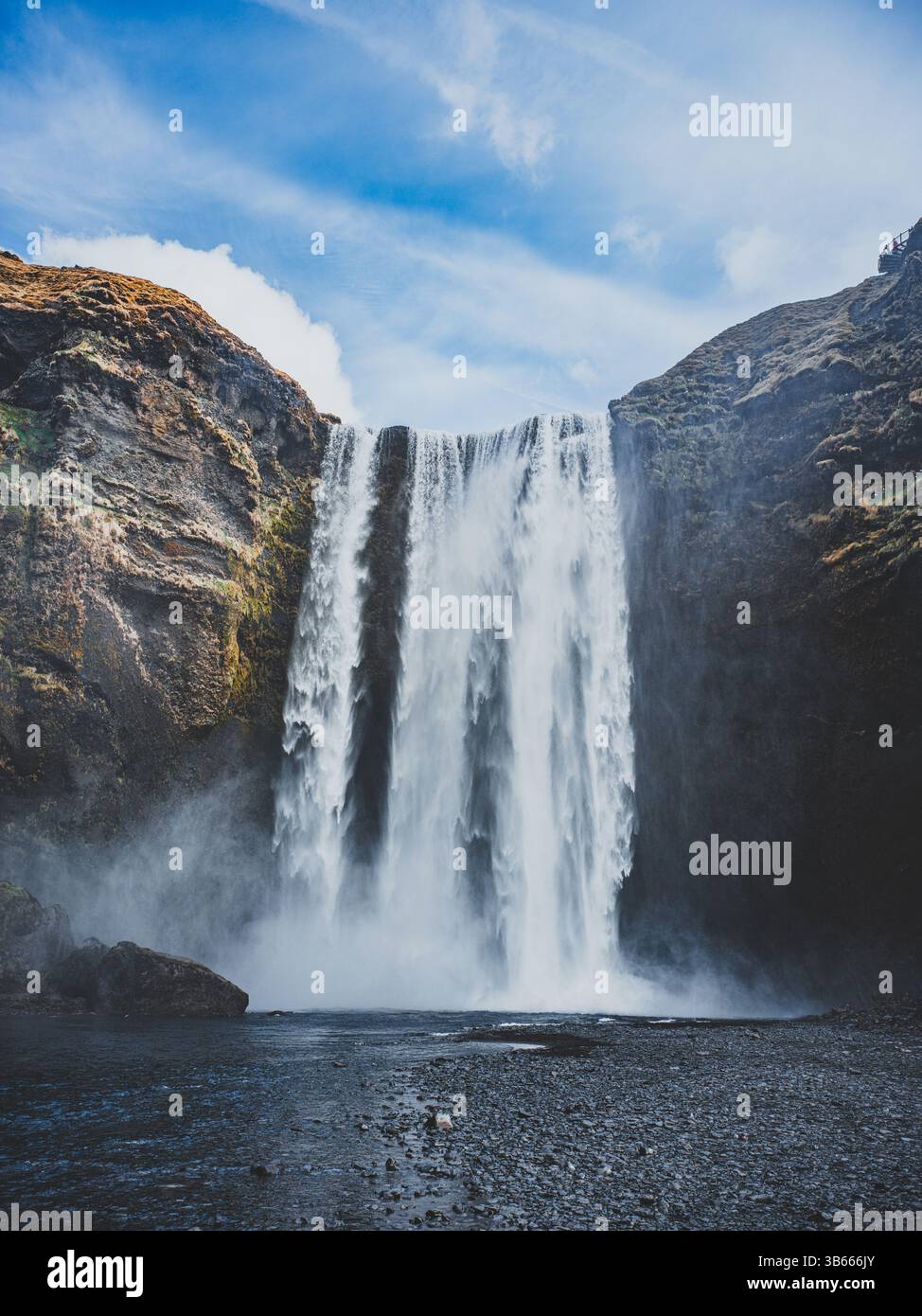 Cascata di Skógafoss che si schianta lungo un'alta scogliera sotto un cielo luminoso, nel sud dell'Islanda Foto Stock
