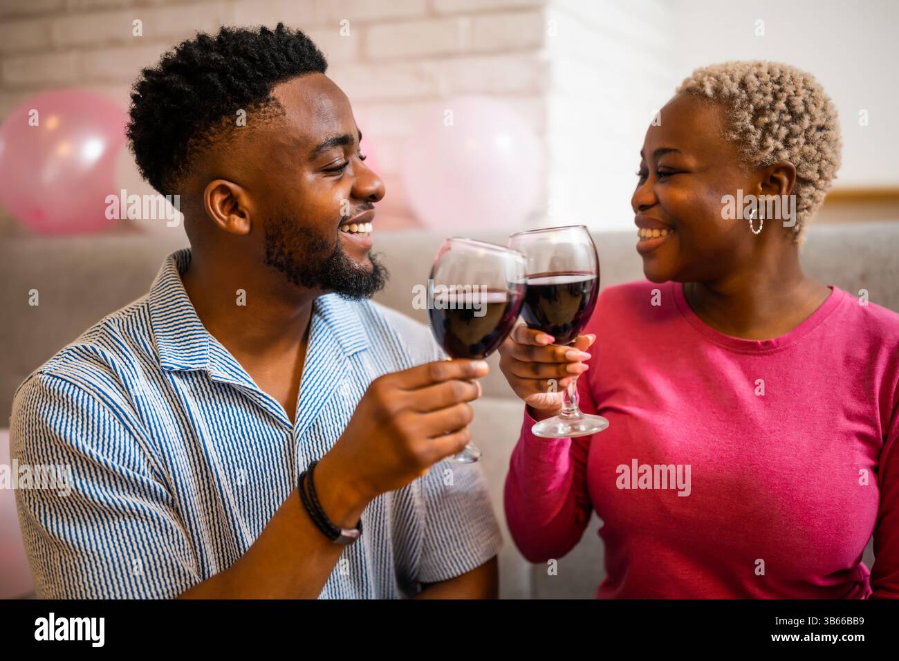 Felice giovane coppia che festeggia il compleanno della donna a casa. Stanno brindando con del vino. Foto Stock