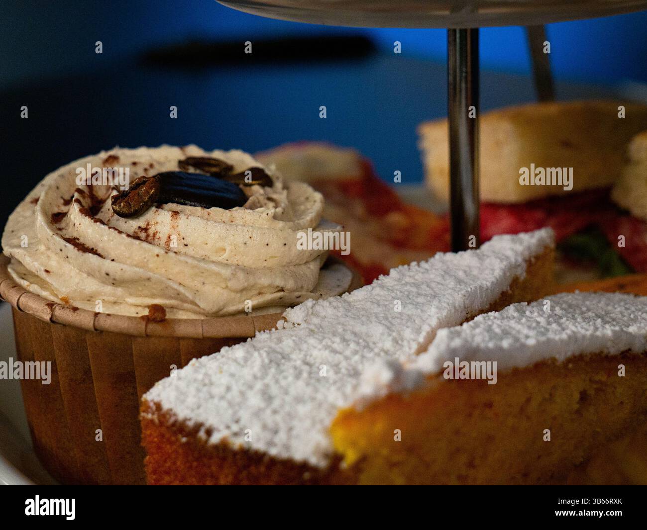 Un dettagliato primo piano di uno stand a due piani con un cupcake decorato e una fetta di torta spolverata di zucchero a velo. Foto Stock