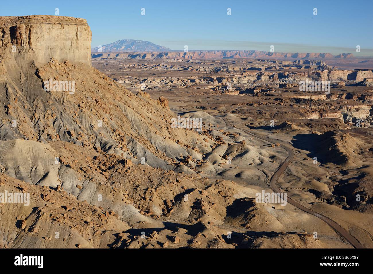 VISTA AEREA. Strada sterrata in un paesaggio desertico con scarpate e calanchi, il monte Navajo in lontananza. Big Water, Kane County, Utah, Stati Uniti. Foto Stock