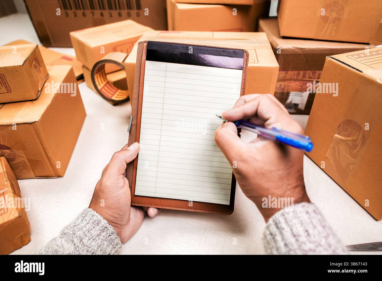 Venditori che controllano le scatole di imballaggio, mani con penna su un blocco note vuoto vicino alle scatole di cartone. Verifica dell'inventario o creazione della distinta di imballaggio. co. e-commerce Foto Stock