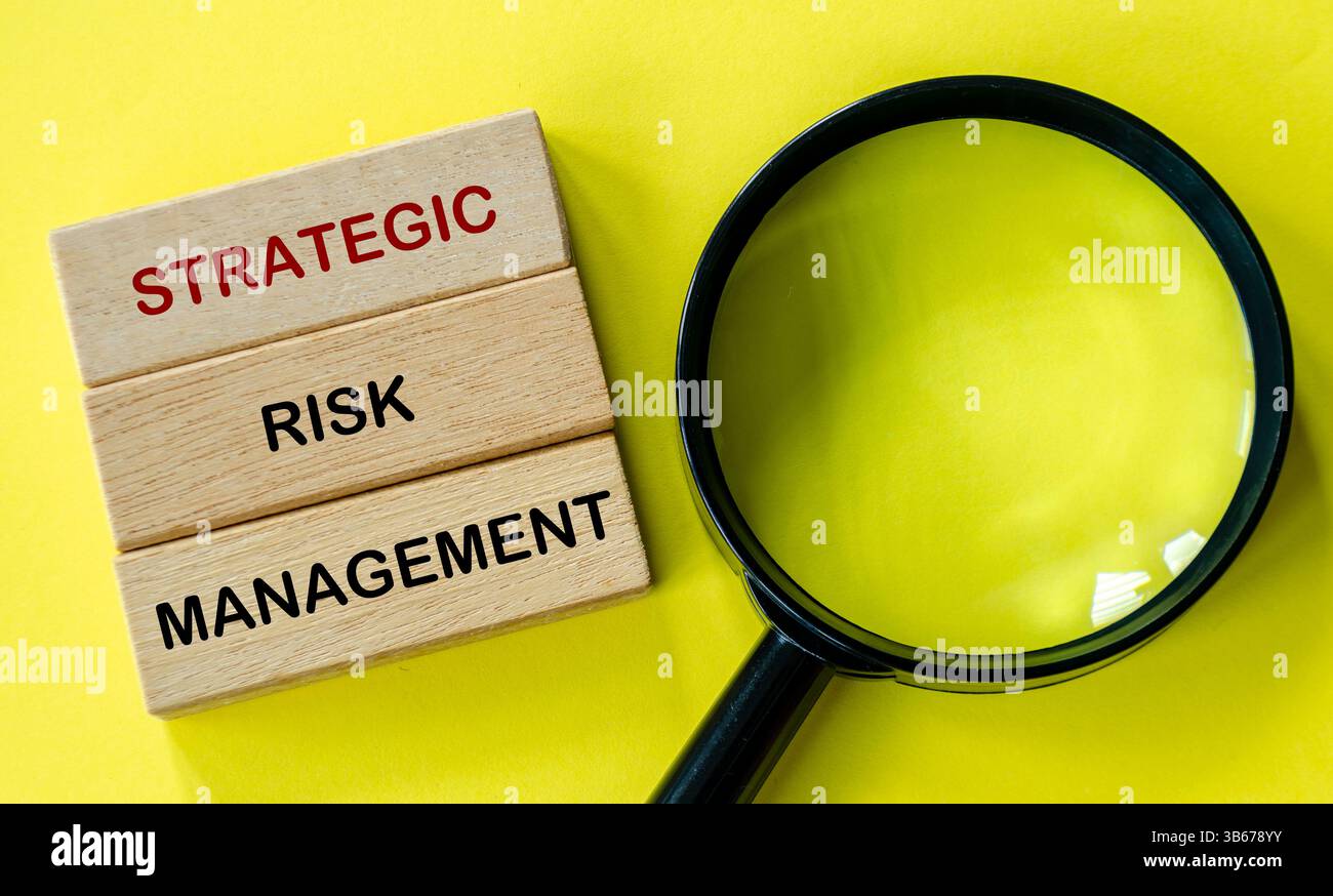 Testo sulla gestione strategica dei rischi su blocchi di legno con lente d'ingrandimento su sfondo giallo Foto Stock