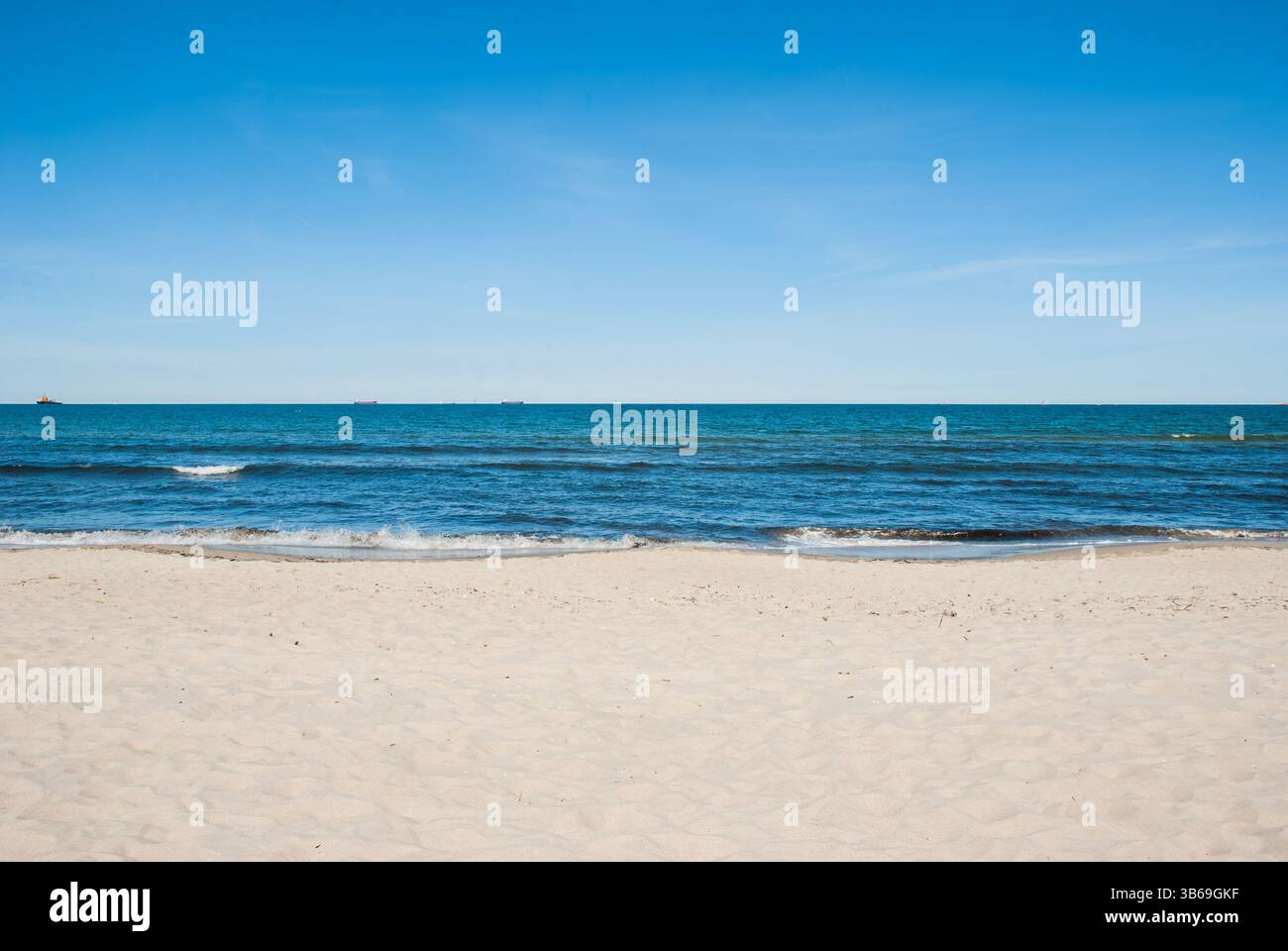 Tranquilla spiaggia con cielo azzurro e onde dolci che si incontrano con la spiaggia sabbiosa in una giornata di sole, catturando la bellezza della costa. Stile di vita digitale nomade. Foto Stock
