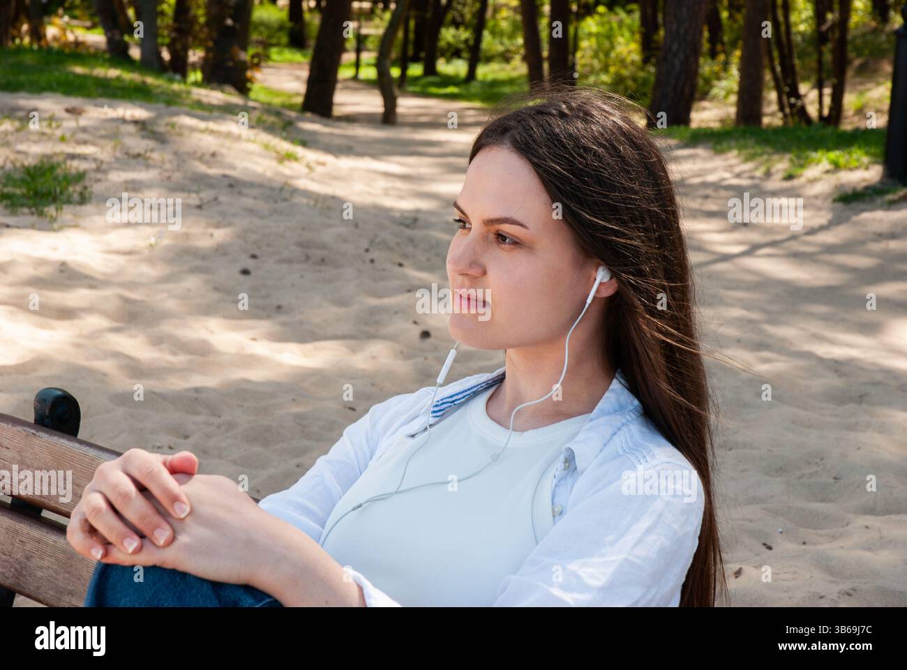 Giovane donna caucasica che si gode un momento di pace nella natura mentre ascolta la musica con le cuffie in un tranquillo parco. Stile di vita digitale nomade. R Foto Stock