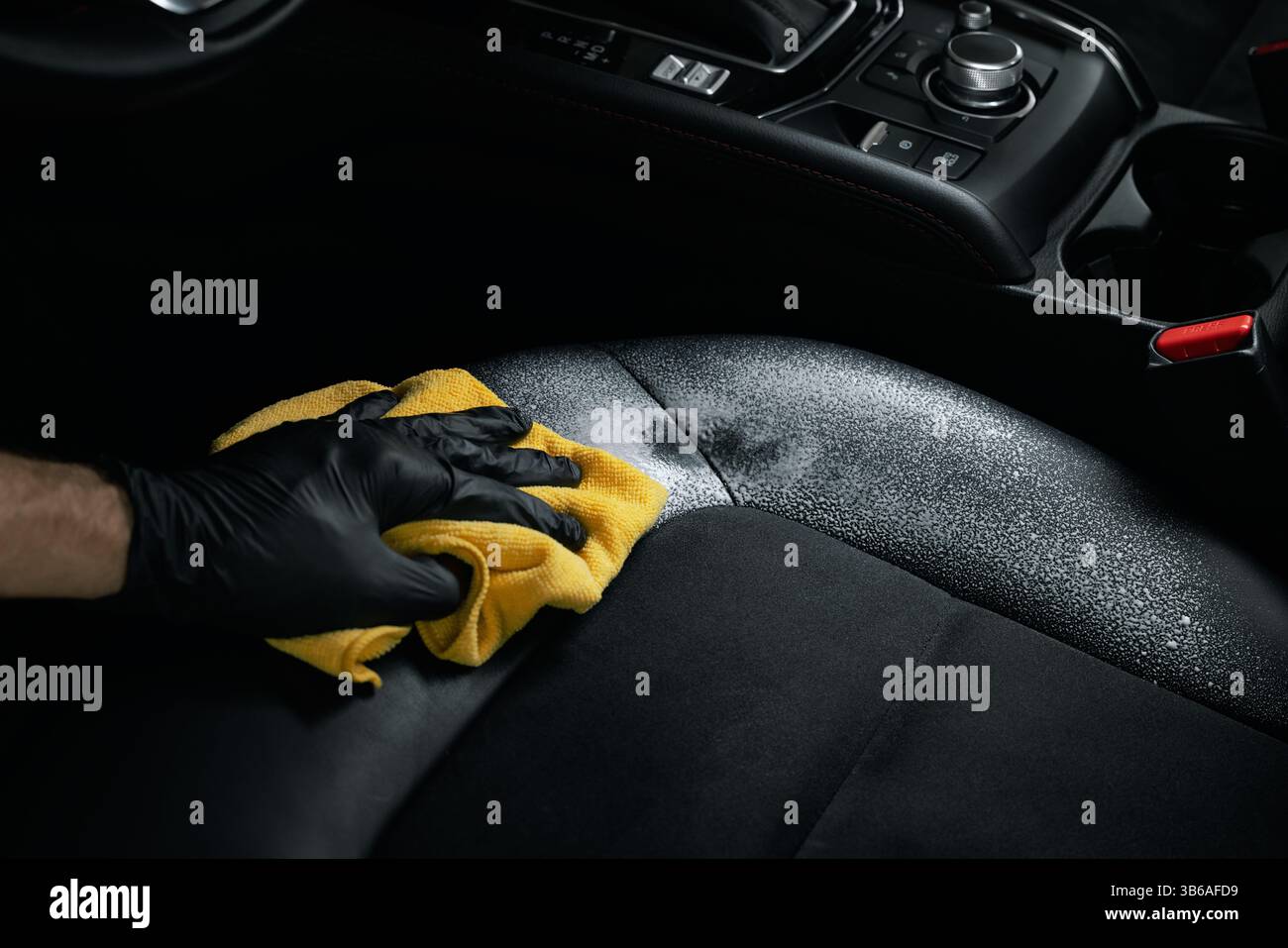 servizio di pulizia e dettaglio degli interni della vettura. uomo che pulisce sedili in pelle alcantara nera con detergente in schiuma e panno in microfibra Foto Stock