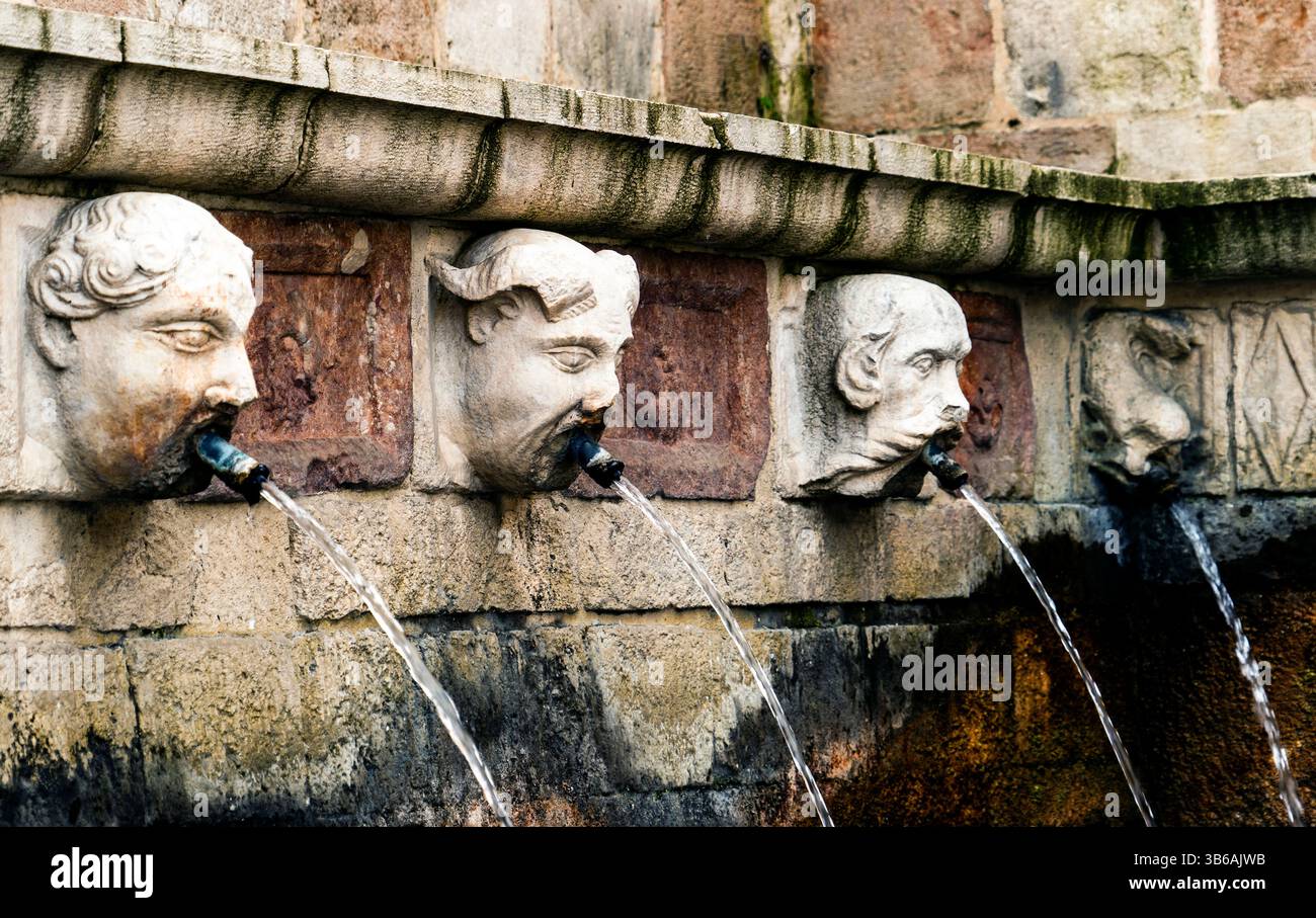 Una storica fontana in pietra con teste scolpite che sprigionano acqua. Le intricate incisioni mostrano espressioni e texture facciali dettagliate, Set aga Foto Stock