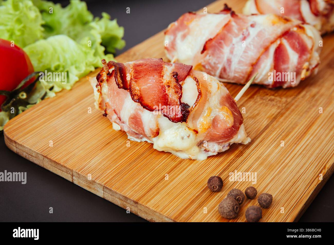 Filetti di pollo cotti avvolti in pancetta croccante e formaggio fuso ripieno serviti su un tagliere di legno. Foto Stock