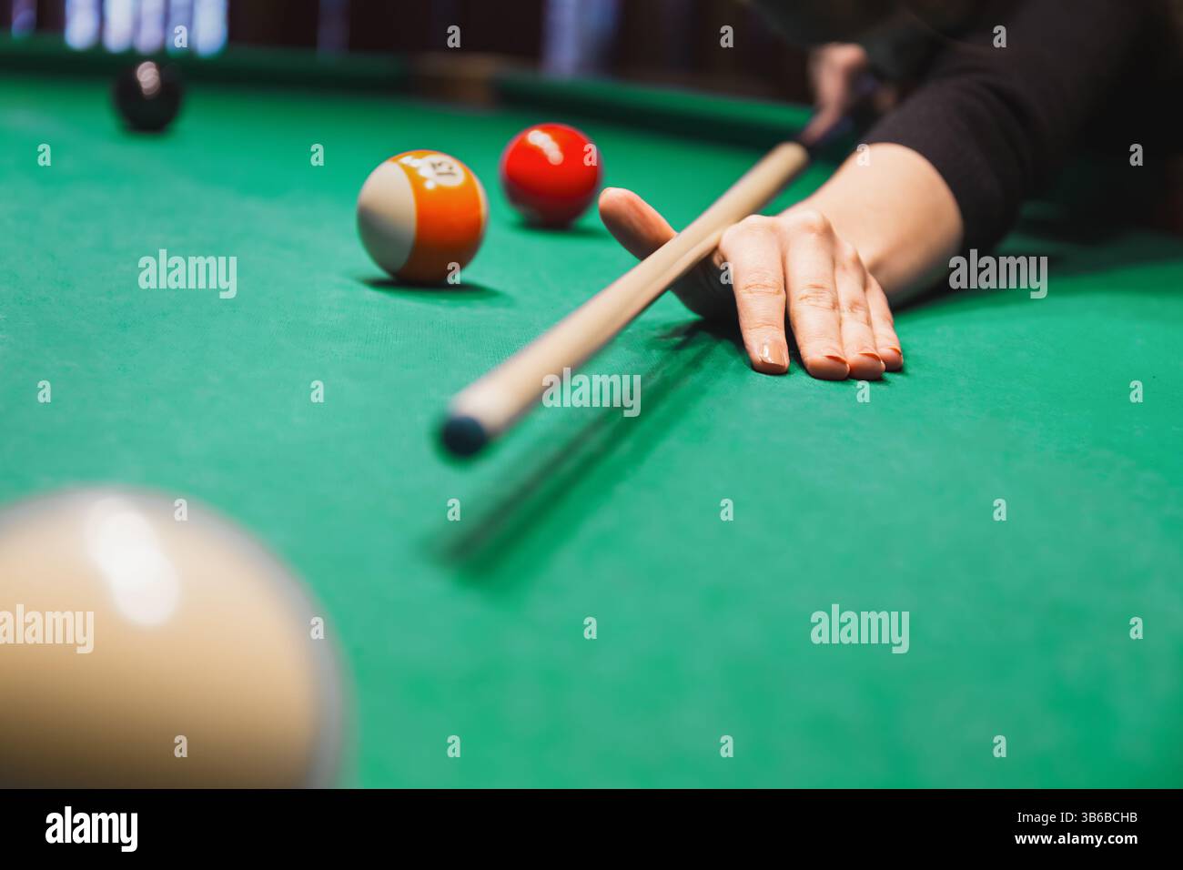 afferrare a mano il tavolo da biliardo e allineare un tiro con il bastoncino vicino alle palle da biliardo. Bar al coperto con giochi Foto Stock