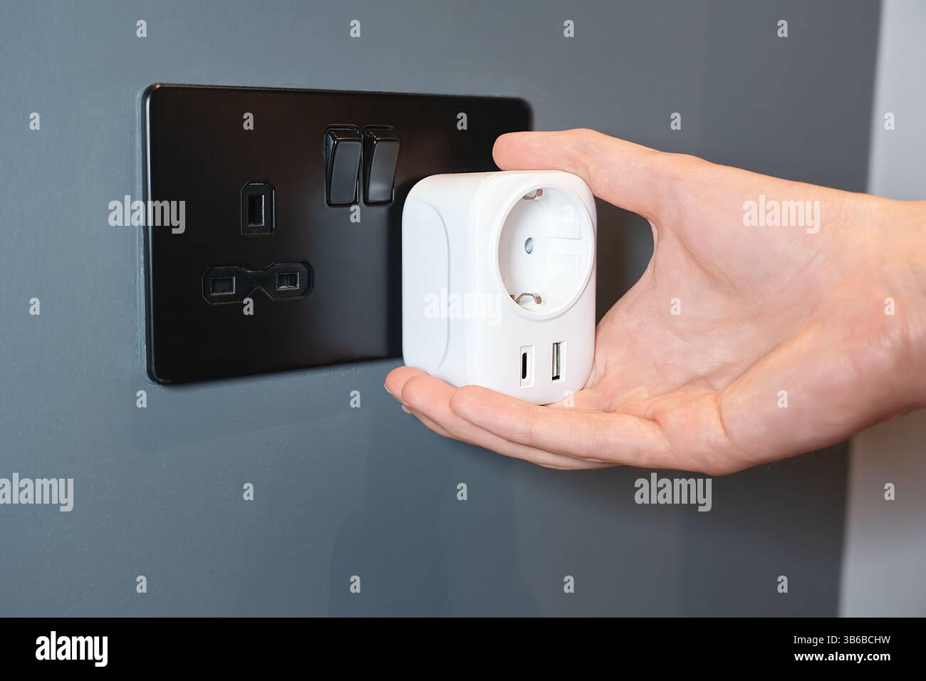 Con una mano si tiene un adattatore UE Smart Power con porte USB accanto a una presa UK nera Foto Stock