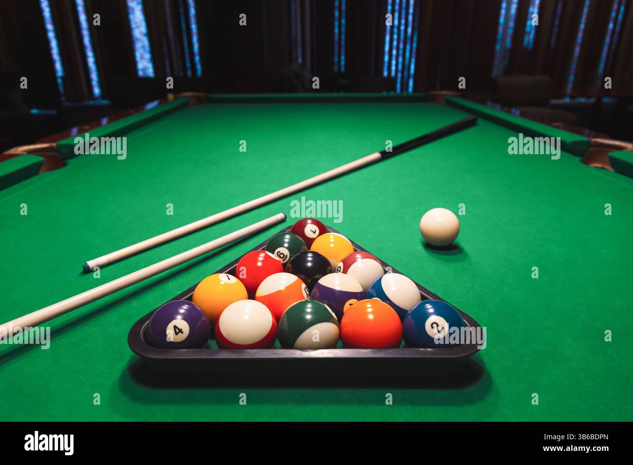 Set completo di palline da biliardo numerate disposte in una cremagliera triangolare con bastoncini su un tavolo da biliardo verde. Giochi da bar, sport di punta Foto Stock