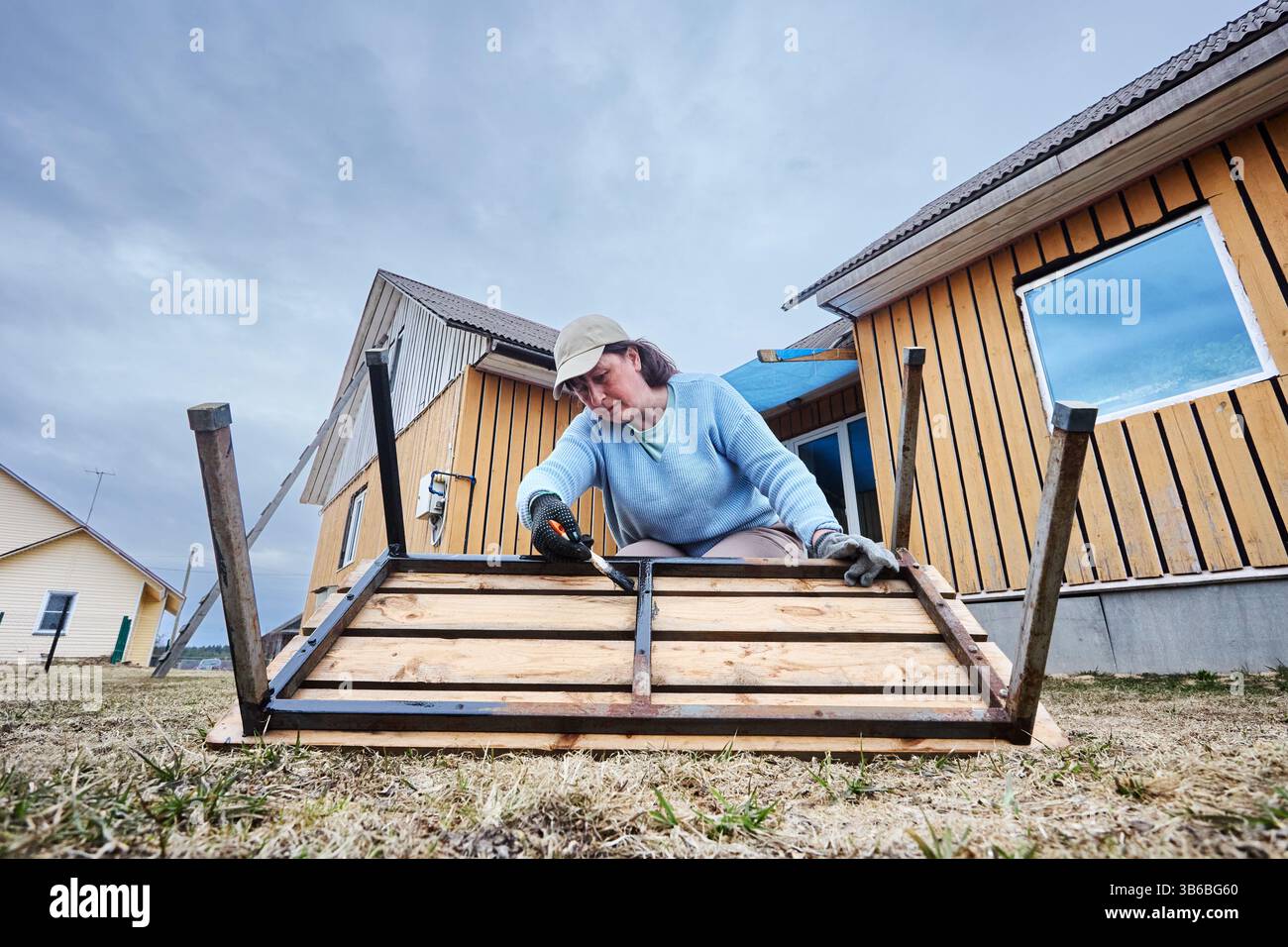 Il pratico hobbista da giardino utilizza una spazzola per applicare uno spesso rivestimento protettivo, concentrandosi su ogni esposizione Foto Stock