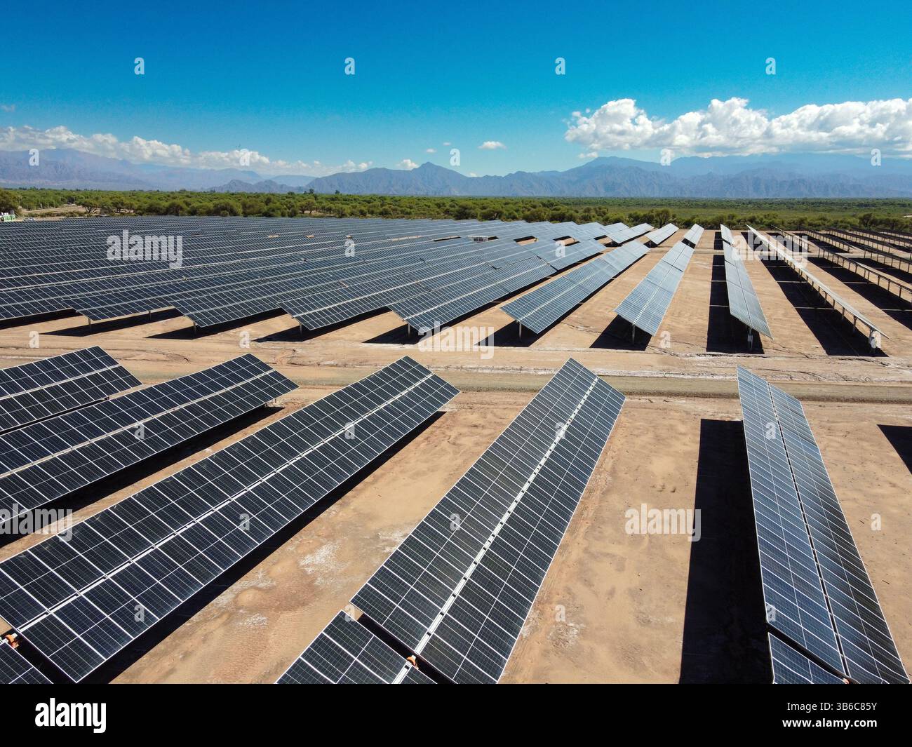 Sotto un cielo parzialmente nuvoloso, estesi campi di pannelli solari si estendono a Tinogasta, con le imponenti Montagne delle Ande che si stagliano in lontananza Foto Stock