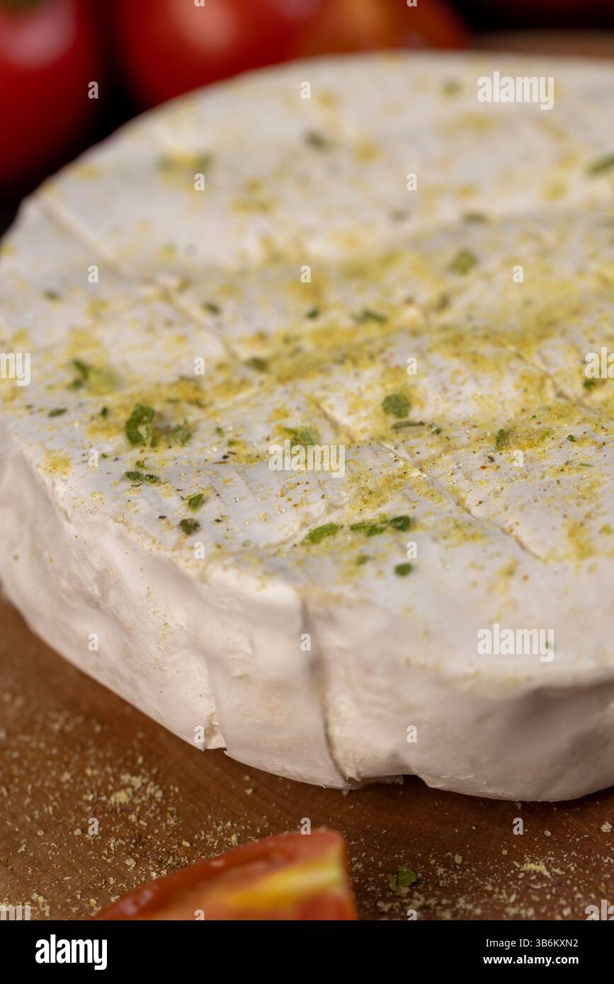 formaggio morbido con muffa cosparsa di spezie e pomodori, formaggio morbido bianco in sale e spezie e piccoli pomodori rotondi rossi sul tavolo, primo piano Foto Stock