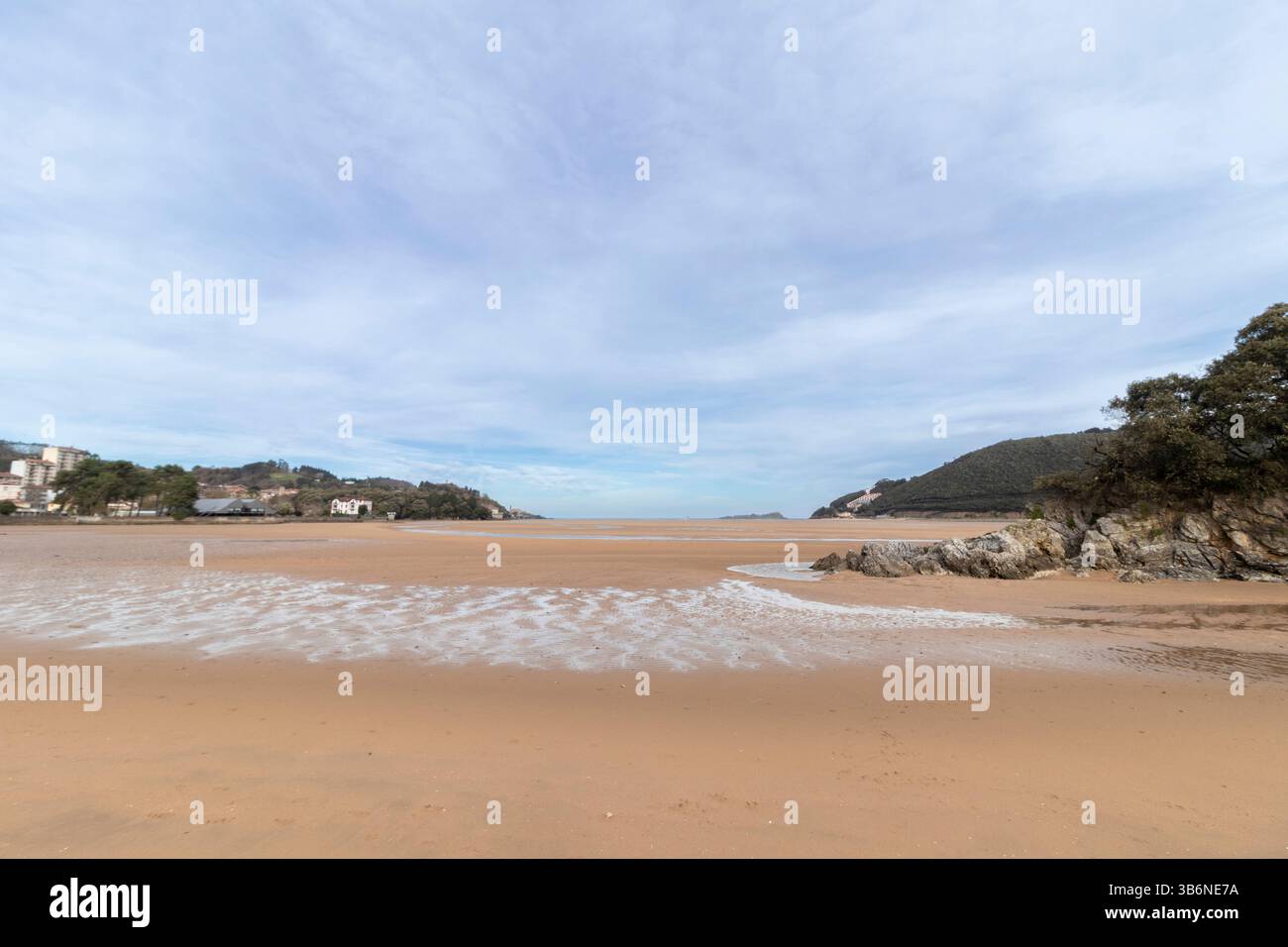 Onde dolci che si infrangono sulla sabbia dorata con la bassa marea, rivelando rocce e creando un tranquillo paesaggio costiero Foto Stock