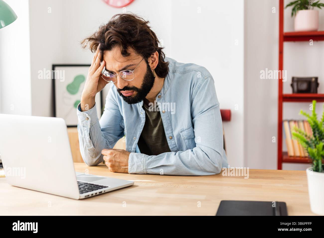 Uomo preoccupato che leggesse cattive notizie sul computer portatile mentre lavorava in ufficio Foto Stock