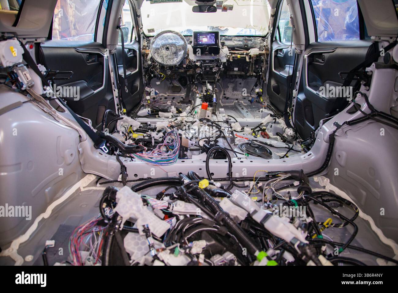 Fasci aggrovigliati di cablaggi automobilistici disordinati all'interno di un abitacolo completamente spogliato Foto Stock