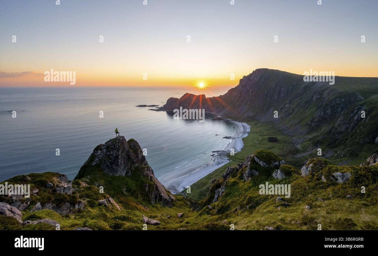 Arrampicati sulle rocce di fronte al pittoresco paesaggio, ammira il paesaggio costiero al tramonto, le scogliere e la cima di Matind o Matinden, la spiaggia di Hoyvika e. Foto Stock